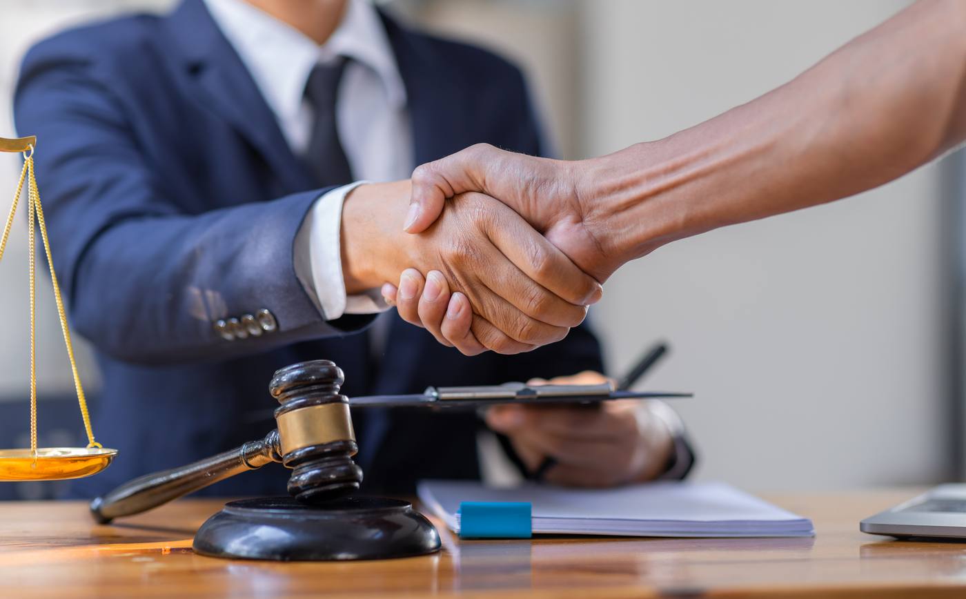Handshake between lawyer and client beside legal scales and gavel